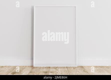 Empty thin white frame on light wooden floor with white wall behind it. Stock Photo