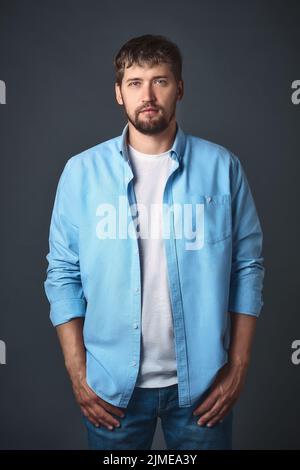 This young confident man with a beard in stylish casual clothes poses in the studio against a gray background. Stock Photo