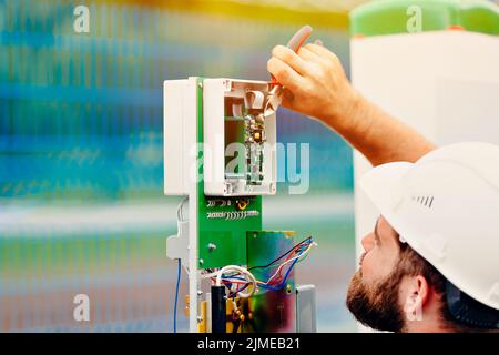A qualified electrical engineer sets up a control and measuring device at an industrial facility on a summer day. Stock Photo