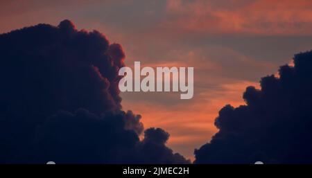 Defocus, a dramatic orange sky between dark thick clouds that are illuminated by a red sunset and hidden behind clouds. Stock Photo