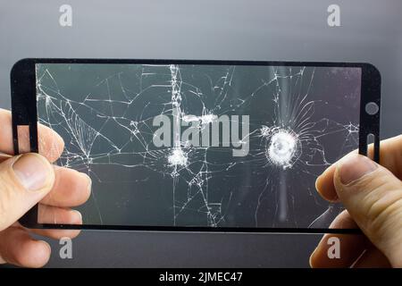 Broken protective glass of smartphone with cracks in hands on black background. Stock Photo