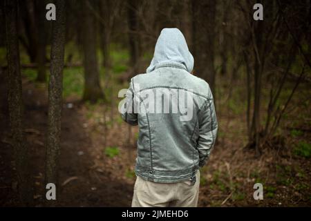 The guy in the hood is taken off the back. A man in jeans stands in the woods. Unknown person from the outside. Stock Photo