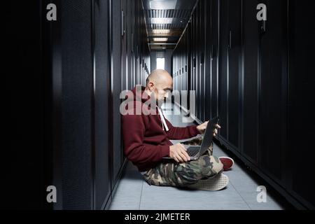 The hacker with a bald head and a beard sits with the computer among ...