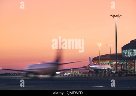 Airplane in blurred motion. Traffic at airport during colorful sunrise. Stock Photo