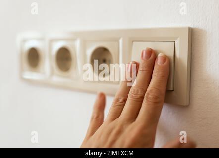 Fingers turn on or off light switch. Saving energy, electricity, power, energy crisis concept. Stock Photo