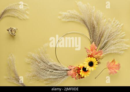Floral wreath from dry pampas grass and Autumn leaves on golden paper. Stock Photo