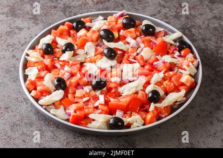 Spanish appetizer salad of salted cod, fresh tomatoes, onions and black olives close-up in a plate on the table. horizontal Stock Photo