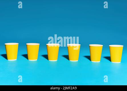 Row of yellow paper cup in line on blue background Stock Photo