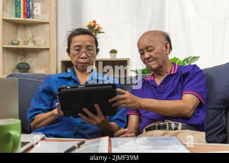 Elderly Asians use tablets and insurance documents at home. Stock Photo