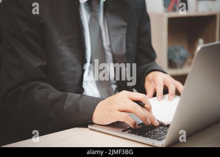 Man person using keyboard computer laptop holding pen and book on desk. Stock Photo