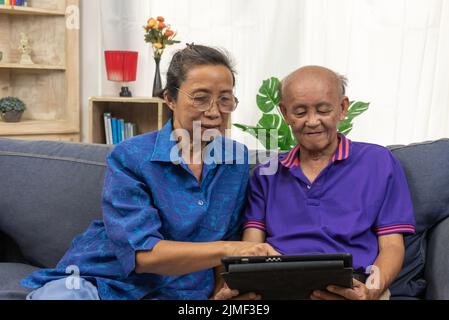 Asian senior using tablet online internet communication technology on sofa at home. Stock Photo