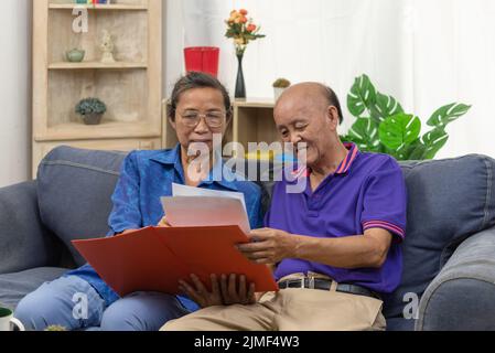 Senior asian couple talking happy planing retirement insurance health care contract on sofa. Stock Photo