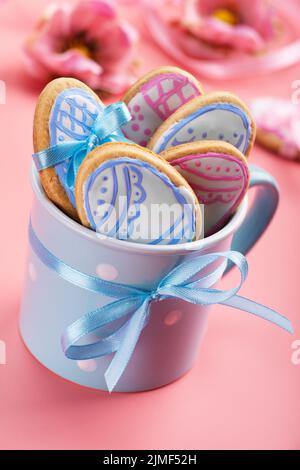 Easter baking background of frosted cookies in shape of egg in blue mug on pink background Stock Photo