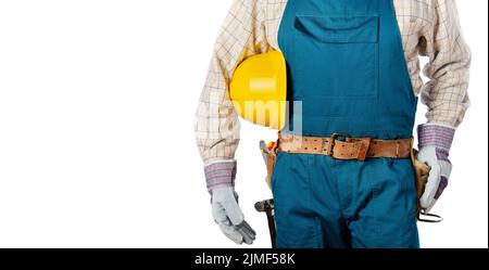 Middle aged contractor in overalls with tool belt holds yellow hard hat in his hands on white background Stock Photo