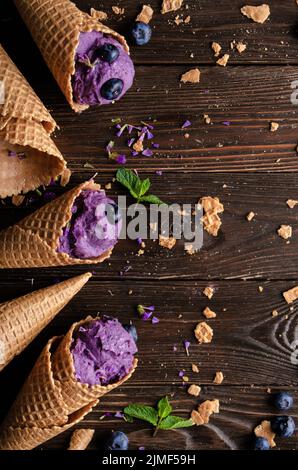 Flat lay view at wafer cones with blackberry icecream on wooden kitchen table Stock Photo