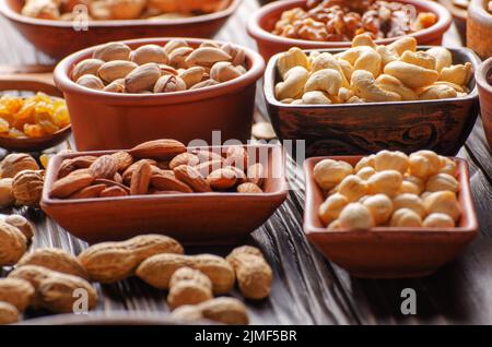 Assorted nuts and seeds in clay bowls on wooden kitchen table Stock Photo