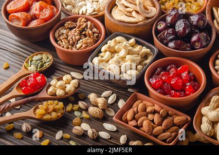 Different nuts seeds and dried fruits in bowls and spoons on wooden kitchen table Stock Photo