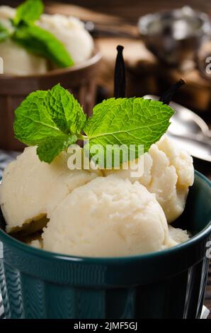 Vanilla icecream balls in clay bowls on wooden kitchen table with ice cream scoop aside Stock Photo