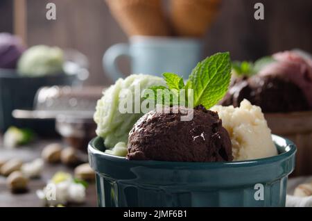 Three scoops of Vanilla pistachio and chocolate icecream balls in clay bowls on wooden kitchen table Stock Photo