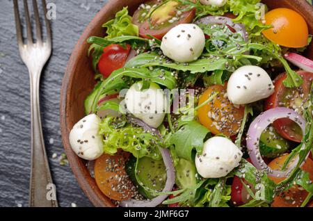 Flat lay of vegetable salad with mozzarella cheese, lettuce, cherry tomatoes, radish, cucumber, onion and basil in clay dish Stock Photo