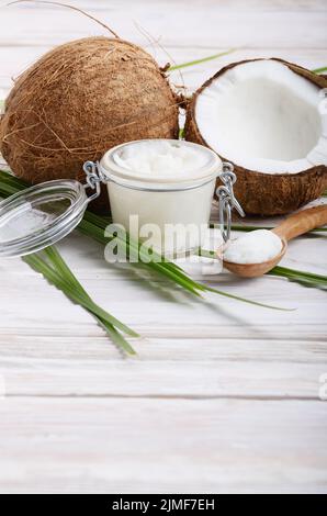 Coconut oil in airtight glass jar spoon and shell pieces on white wooden table Stock Photo