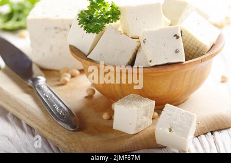Soy Bean curd tofu in wooden bowl on white wooden kitchen table. Non-dairy alternative substitute for cheese. Place for text Stock Photo