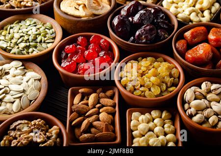 Assorted nuts seeds and dehydrated fruits in bowls on wooden kitchen table Stock Photo
