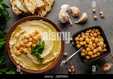 Hummus topped with chickpeas, olive oil and green coriander leaves on stone table with pita bread aside Stock Photo