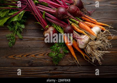 Vegetarian background of fresh organic beetroots green garlic and carrots on kitchen wooden rustic table Stock Photo