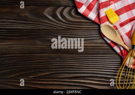 Red checkered napkin and kitchen utencils on brown wooden kitchen table with copy-space. Top view Stock Photo
