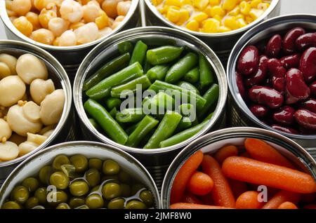 Canned vegetables in opened tin cans on kitchen table. Non-perishable long shelf life foods background Stock Photo