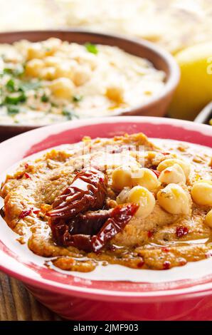 Fresh homemade Hummus in clay dish topped with olive oil, chickpeas, spices and sun dried tomatoes on stone table Stock Photo