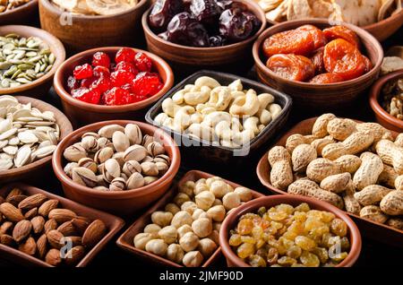 Different nuts seeds and dried fruits in bowls on wooden kitchen table Stock Photo