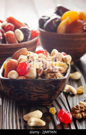 Assorted nuts and dried fruits in clay bowl on wooden kitchen table closeup Stock Photo