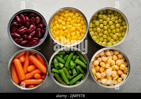 Flat lay view at canned carrots, chickpeas, kidney beans, green beans, peas and corn in opened tin cans on kitchen table. Non-pe Stock Photo