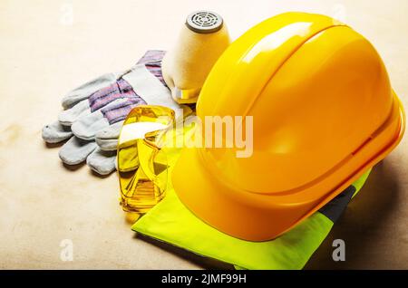 Yellow plastic hard hat, glasses, respirator and protective gloves laying on plywood. Safe labor concept Stock Photo