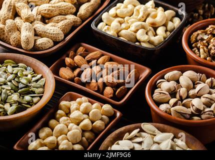 Assorted nuts and seeds in clay bowls on wooden kitchen table Stock Photo