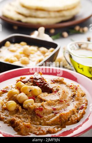 Fresh homemade Hummus in clay dish topped with olive oil, chickpeas, spices and sun dried tomatoes on stone table Stock Photo