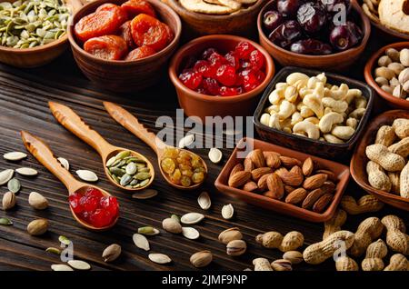 Nuts seeds and dried fruits in bowls and spoons on wooden kitchen table food background Stock Photo