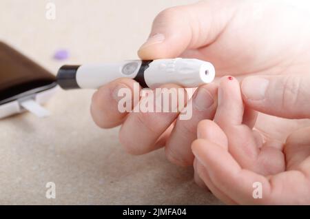 Man Pierce his fingertip before doing blood test with personal glucometer Stock Photo
