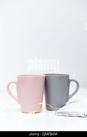 Two pink and grey coffee mugs mockup and a bar of chocolate on white background with small golden lights and bokeh. Blank template for your design, branding, business. Stock Photo