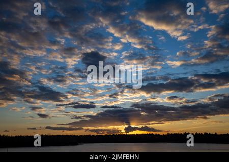 Epic red, blue and golden clouds above the forest lake at sunrise. Dramatic colorful cloudscape. Symmetry reflections on the wat Stock Photo
