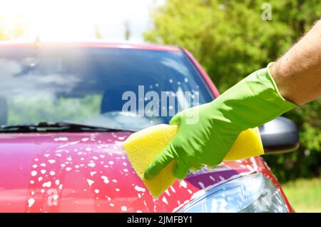 Male hand in green glove with yellow sponge washing car Stock Photo