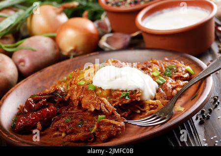 Homemade tasty potato pancakes in clay dish with sun-dried tomatoes and sour cream Stock Photo