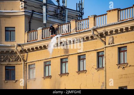 Russia, St. Petersburg, 07 December 2021: The work of utilities to remove snow from the roofs of houses, a man throws off the sn Stock Photo