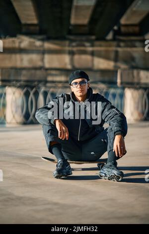 Skater male relax sitting on skateboard on street urban background Stock Photo