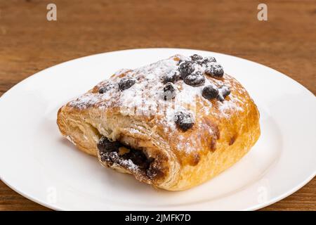 Danish Pasty filled with chocolate cream topping with chocolate chips and icing sugar in white ceramic dish. Stock Photo