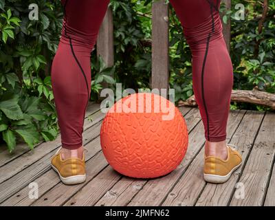 male in compression pants is exercising with a heavy slam ball on a backyard deck, functional fitness and backyard gym concept Stock Photo