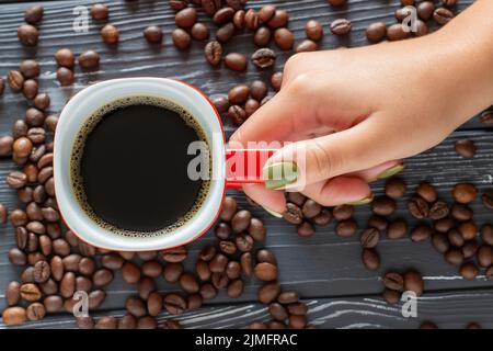 Female hand holding a cup of coffee on a background of coffee beans lying on the table Stock Photo