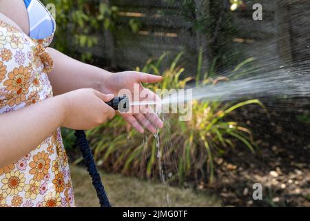 Young Woman waters garden with a hosepipe before the hosepipe ban comes into force due to drought water shortage and poor rainfall. Stock Photo